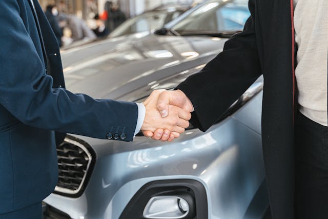 People_shaking_hands_in_suits_car_gray Two hands of people wearing suits shaking in front of a silver car